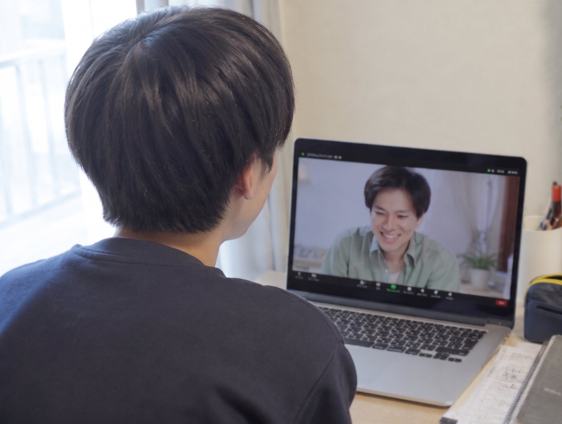自宅の机でノートパソコンを開いて話している子どもと、画面越しに笑顔で話を聴いているメンター